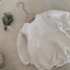 amy rompertje voor baby's en dreumes van 12 en 18 maanden van gewafelde katoenen stof met pofmouwtjes kanten randje langs de hals en knoopjes onderaan liggend op hanger