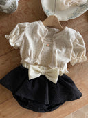 Baby meisje Louve bloomer rokje in zwart met creme kleurige stik en tailleband voor baby's en dreumes van 3 - 18 maanden liggend met isabelle top en vestje vooraanzicht