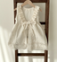 Baby meisje Marie wikkel jurkje/overjurkje schortje van opengewerkt katoen met volantkraag , strik en geborduurde bloemetjes in creme - one size 86/92/98 hangend vooraanzicht 