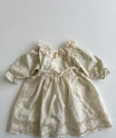 Baby meisje Marie wikkel jurkje/overjurkje schortje van opengewerkt katoen met volantkraag , strik en geborduurde bloemetjes in creme - one size 86/92/98  over jurkje bovenaanzicht 