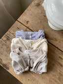 Isabella vestje met pofmouwtjes, elastieke middeltje en knoopje voor baby's van 3 maanden tot 2,5 jaar in drie kleuren lavender, zacht grijs en creme met bloemetjes opgevouwen op tafel bovenaanzicht 