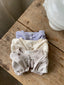 Isabella vestje met pofmouwtjes, elastieke middeltje en knoopje voor baby's van 3 maanden tot 2,5 jaar in drie kleuren lavender, zacht grijs en creme met bloemetjes opgevouwen op tafel bovenaanzicht 