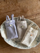 Luchtig en charmant katoenen tanktopje voor baby's van 3 maanden tot 2,5 jaar met schattig bloemetje voorop, bewerkte randjes in drie kleuren, lavender, zacht grijs en creme met bloemtjes liggend bovenaanzicht