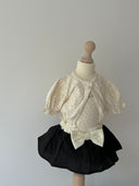 Isabella vestje met pofmouwtjes, elastieke middeltje en knoopje voor baby's van 3 maanden tot 2,5 jaar in creme kleur met bloemetjes met bijpassende tanktop en zwarten louve bloomer met creme tailleband en grote strik op pop