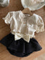 Luchtig en charmant katoenen Isabella tanktopje met bijpassend vestje voor baby's van 3 maanden tot 2,5 jaar in creme met bloemtjes liggend met zwarte louve bloomerrokje met creme kleurige tailleband en grote strik