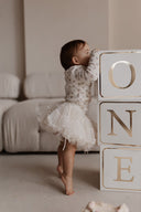 Baby meisje Celina top van geribbeld zacht katoen in creme met bloemenprint en gerimpelde afwerking afgebeeld op babymeisje van de zijkant op teentjes 