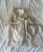 Baby meisje Marie wikkel jurkje/overjurkje schortje van opengewerkt katoen met volantkraag , strik en geborduurde bloemetjes in creme - one size 86/92/98 met lucie broek en blouse liggend bovenaanzicht 