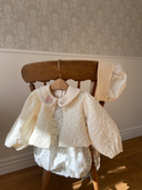 Faye romper zonder mouwen met schattig blauw bloemenprintje met creme kleurig eden jasje eroverheen hangend aan een stoel